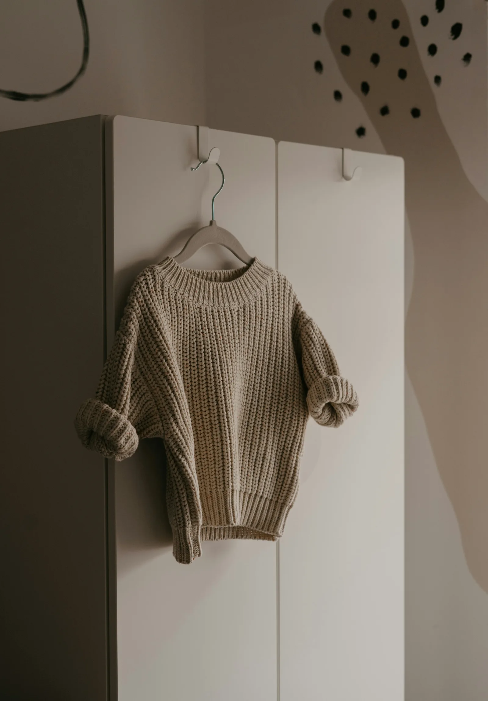 An oatmeal crew-neck jumper on a wooden hanger.