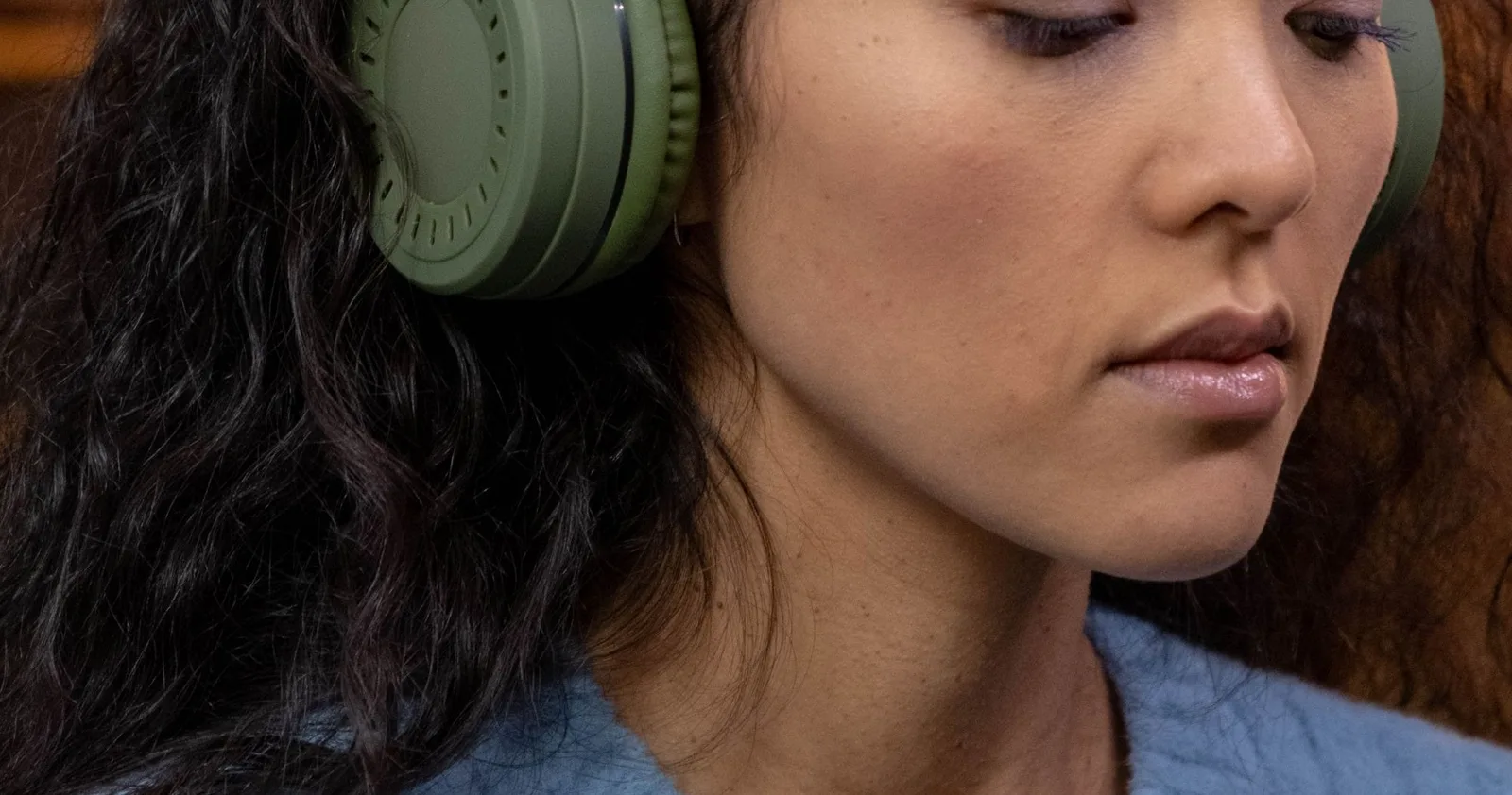A woman in a sage jumper with her headphones on