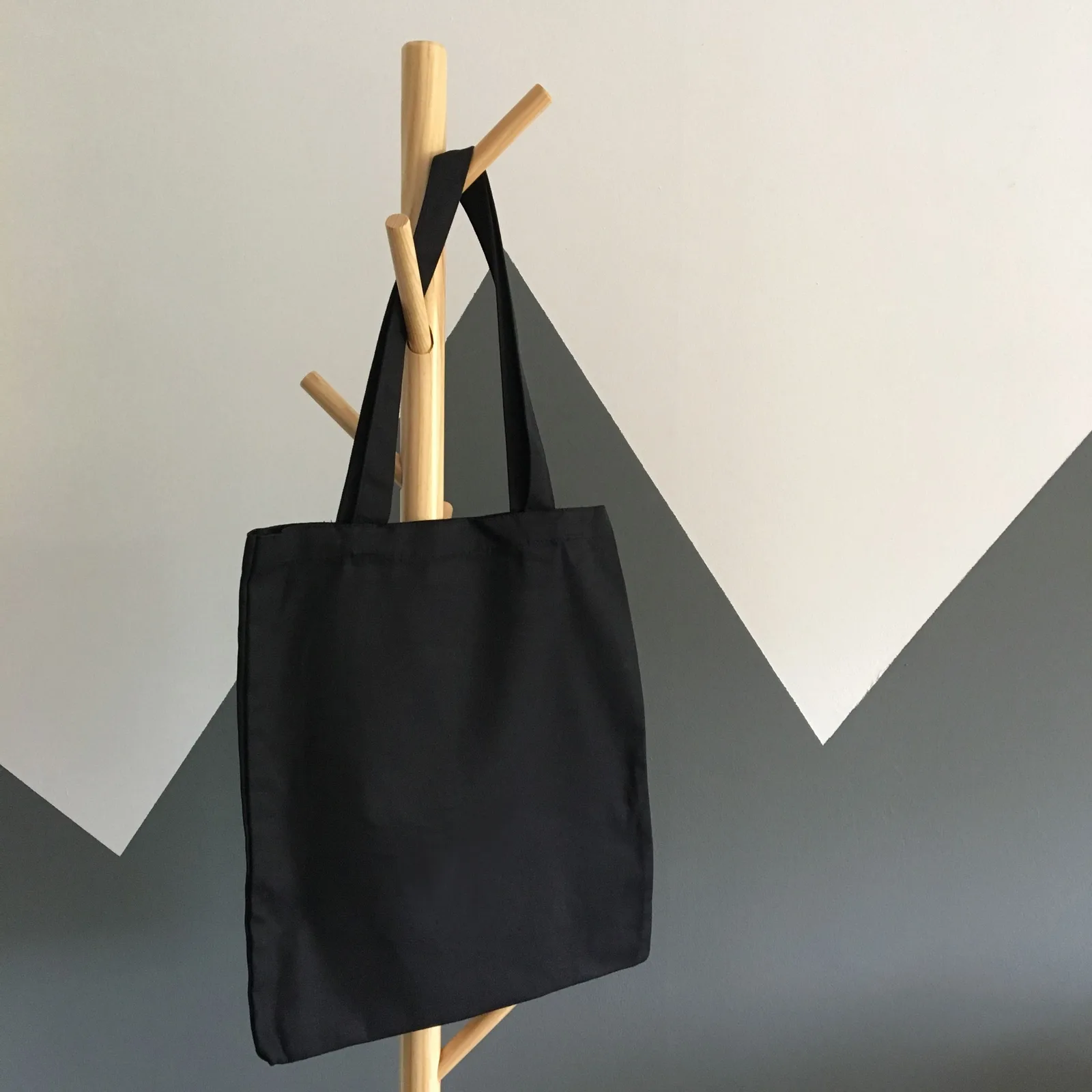 A charcoal canvas tote hanging from a wooden coat rack.