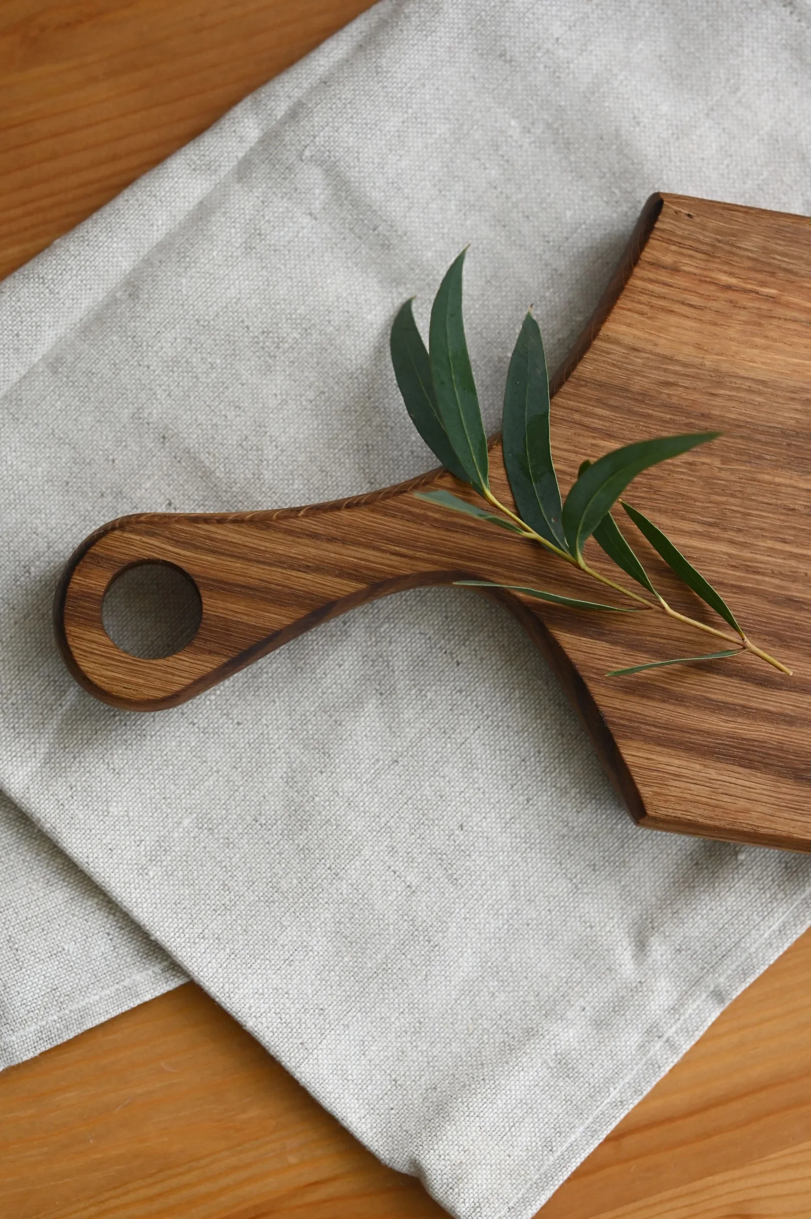 A dark-grained wooden serving board on linen, with an olive sprig.