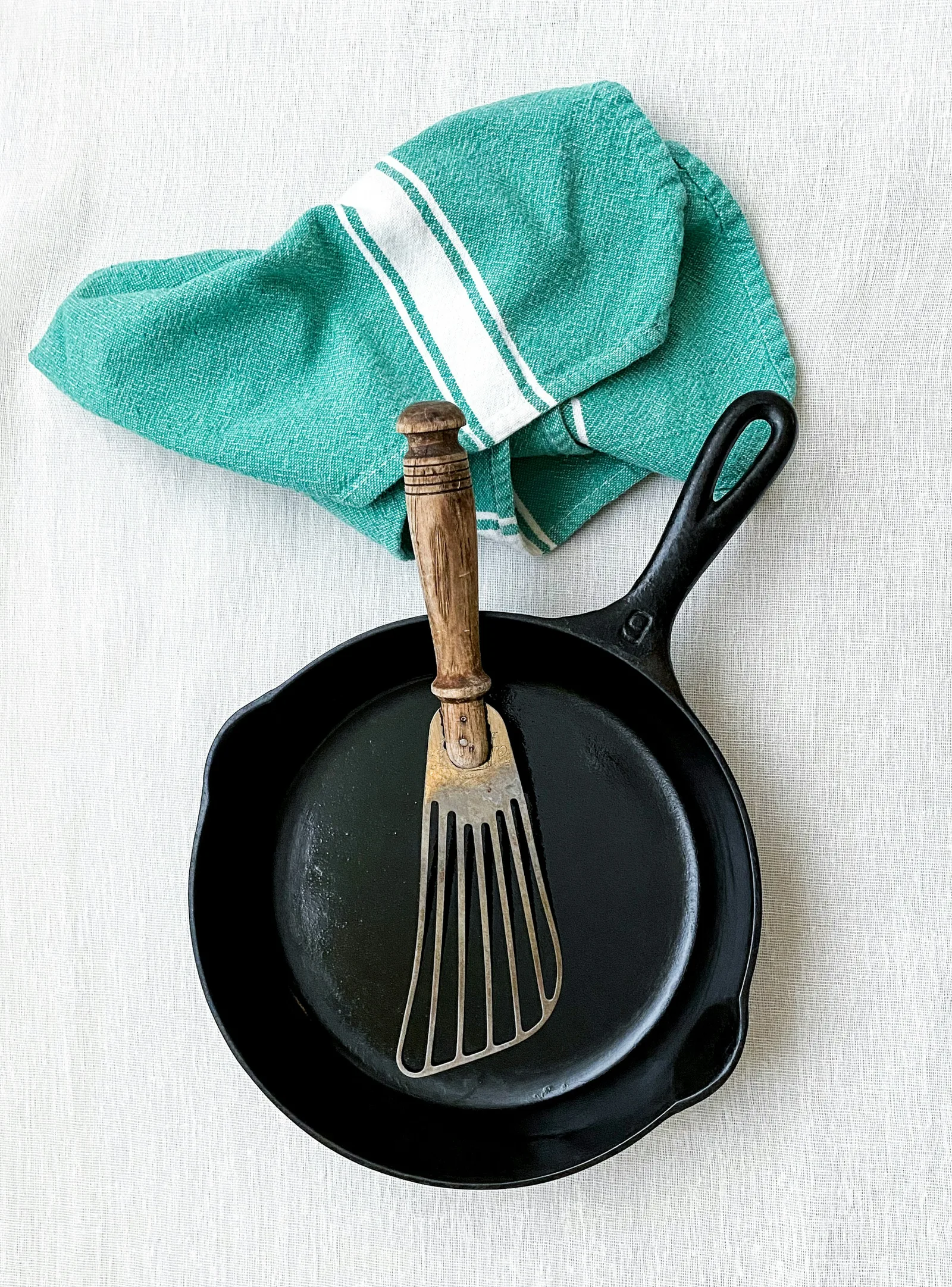 A cast iron skillet seen from above on white linen, a wooden spatula resting in it.