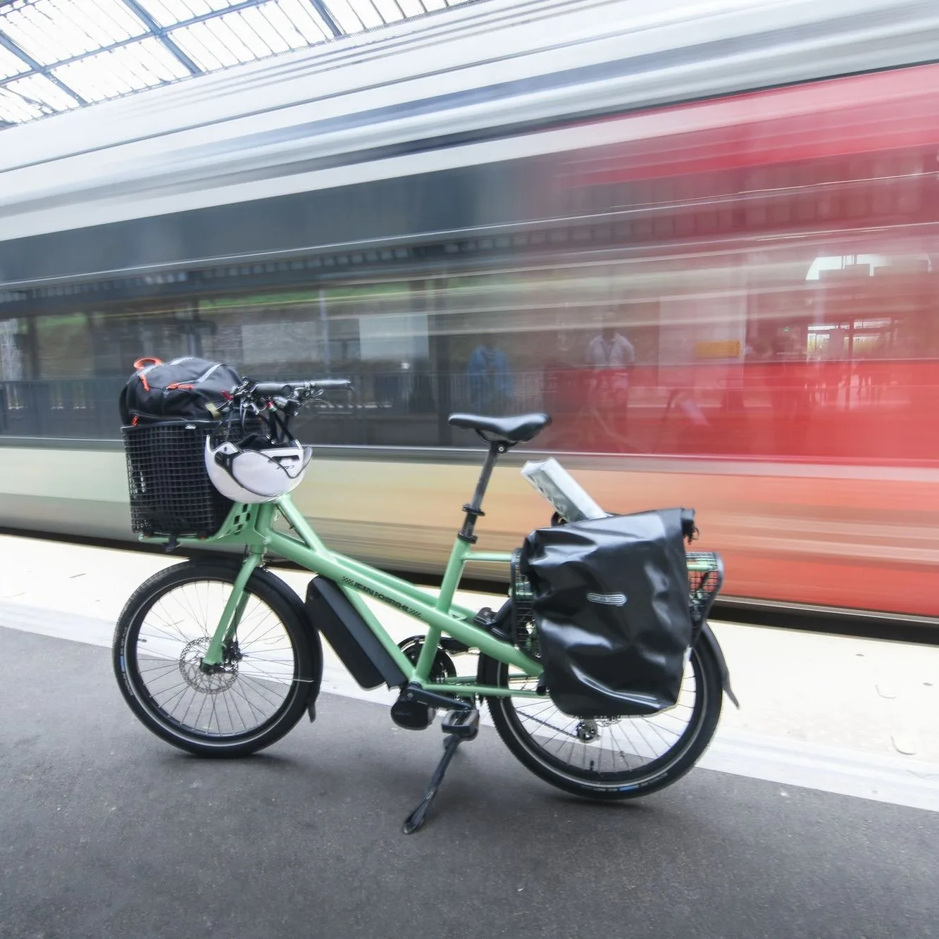 Sage green e-bike with panniers on a station platform