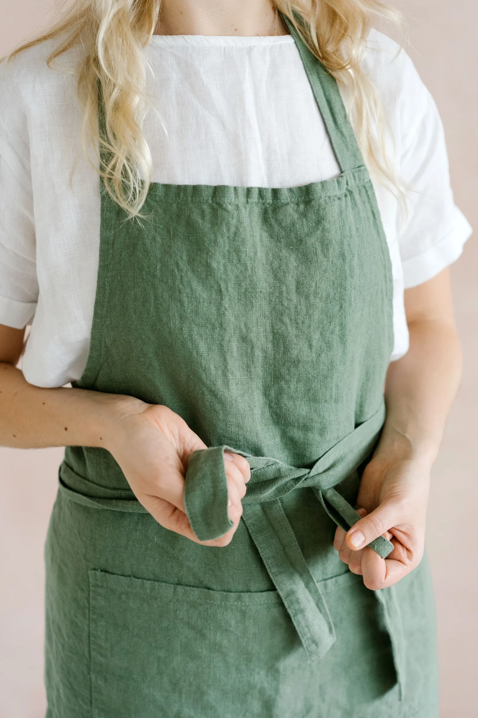 A washed green linen apron, worn, being tied at the waist.